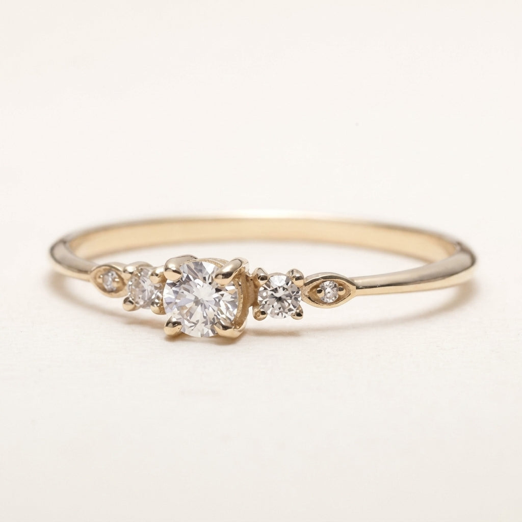 A delicate yellow gold ring featuring a central round-cut clear gemstone flanked by smaller accent stones, set on a plain light background.