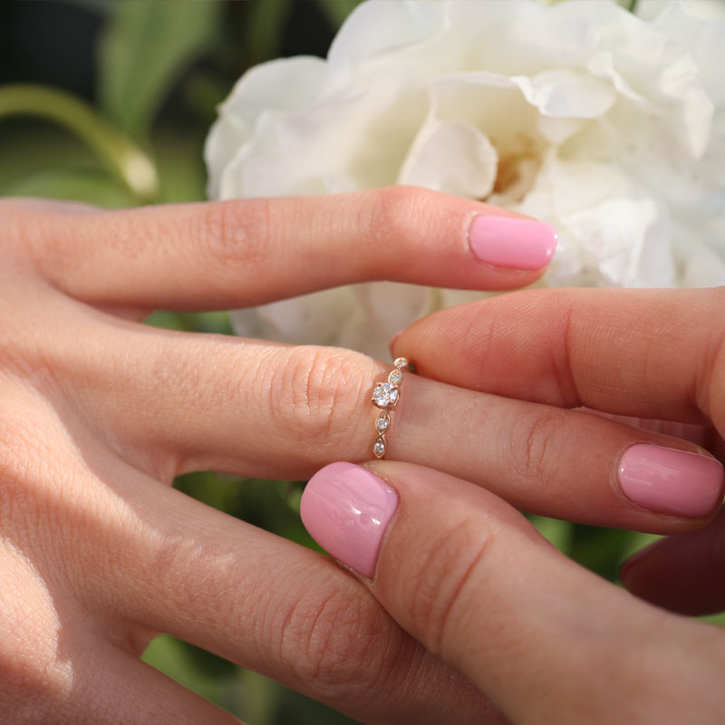 14K white gold pre-engagement ring with round-cut diamond at white background on models hand with white rose flower on backgraund