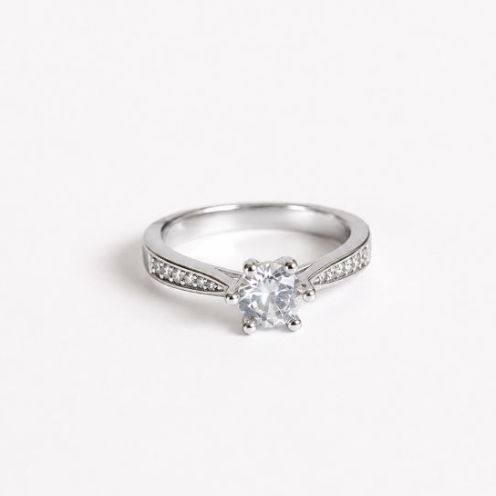 A silver solitaire engagement ring with a round-cut center stone and a pavé-set band, shown on a plain white background.1