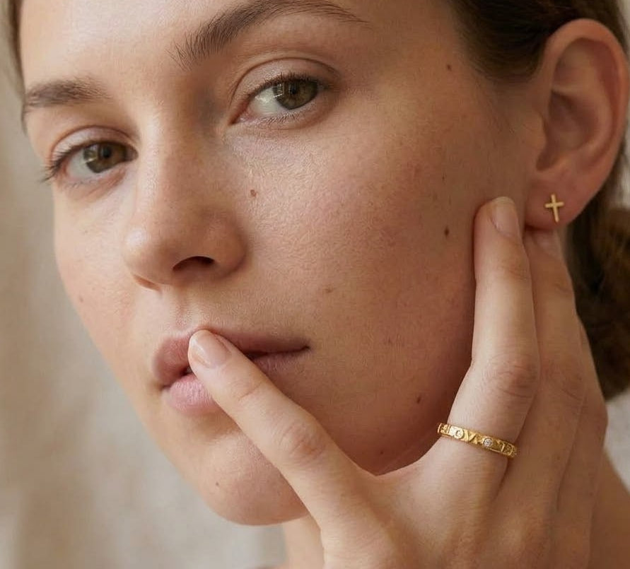 Close-up of a woman wearing gold earrings and a ring, with a neutral background
