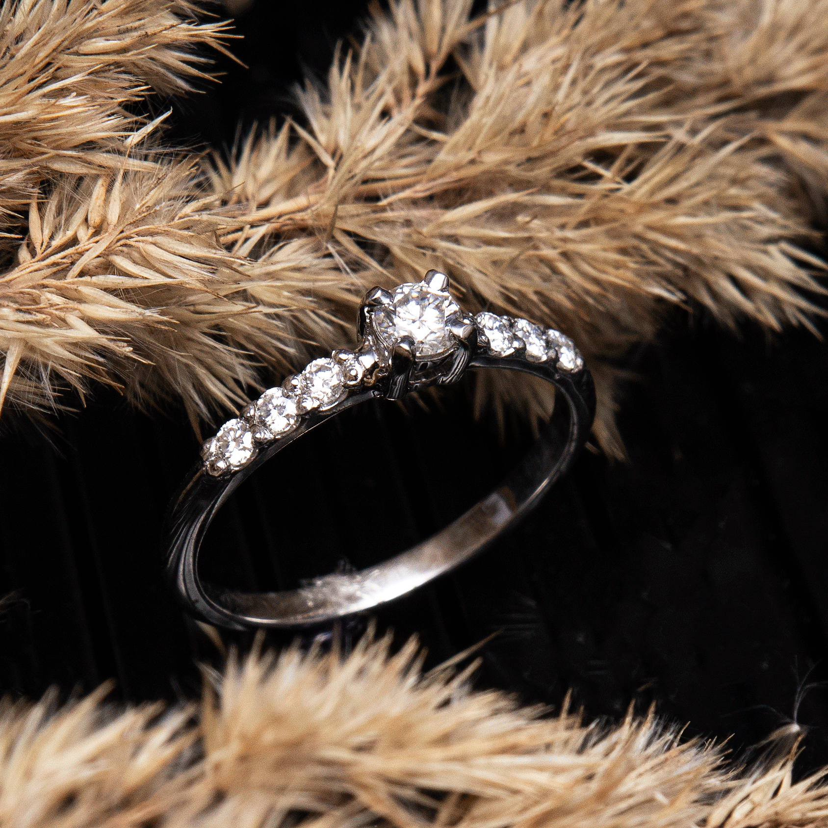 Dainty silver moissanite promise ring with 925 sterling silver band on black background with yellow plants side view