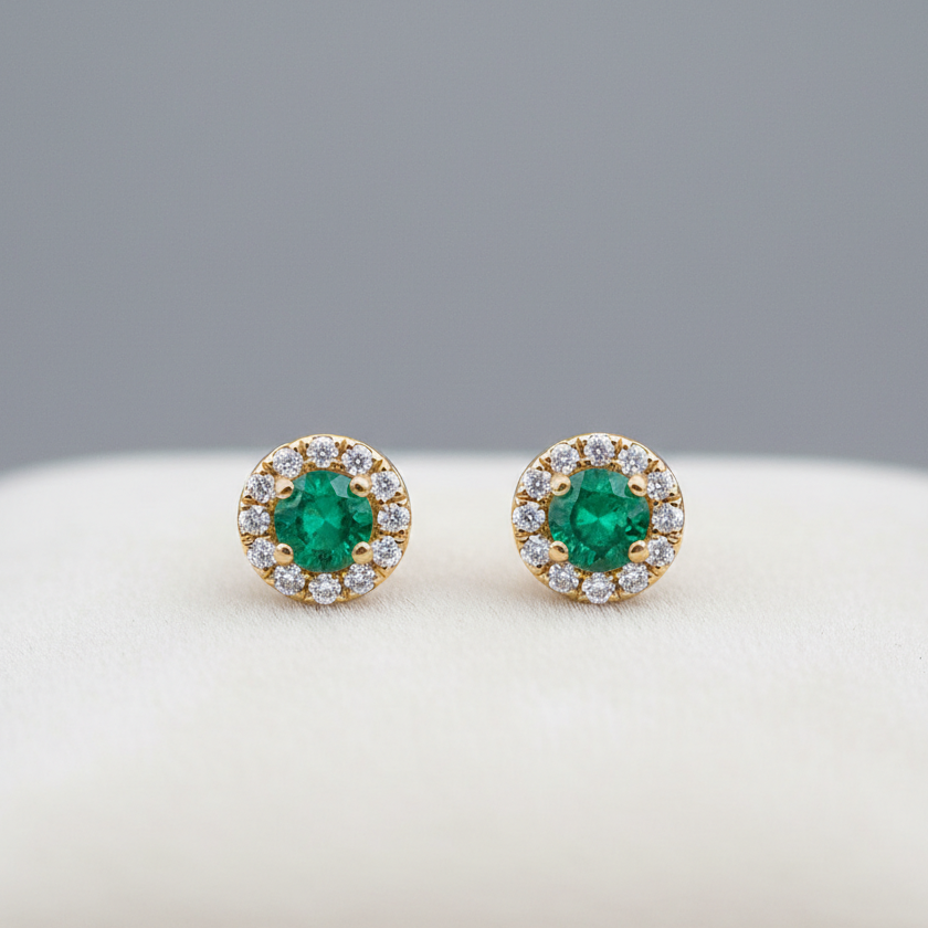 Pair of emerald stud earrings with gold and diamond accents on a white surface.