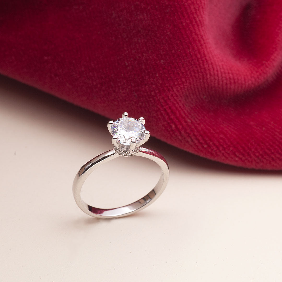 A white gold engagement ring with a large round moissanite set against a red velvet background.