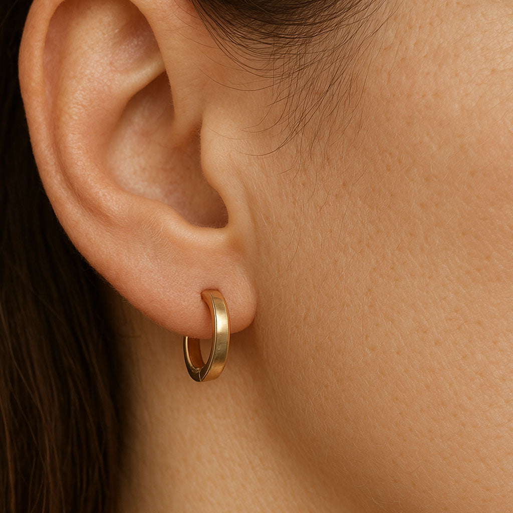 Gold huggie hoop earring worn on a woman's ear, shown in close-up on natural skin tone background
