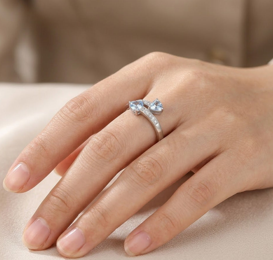 Hand wearing a silver ring with blue gemstones on a beige background