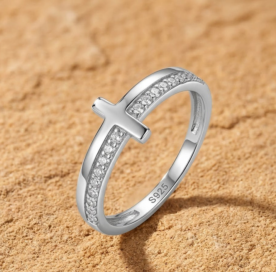 Silver cross-shaped ring with CZ on a sandy background