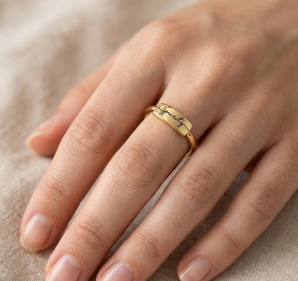 Silver gold-plated ring with engraved text on a hand against a beige fabric background