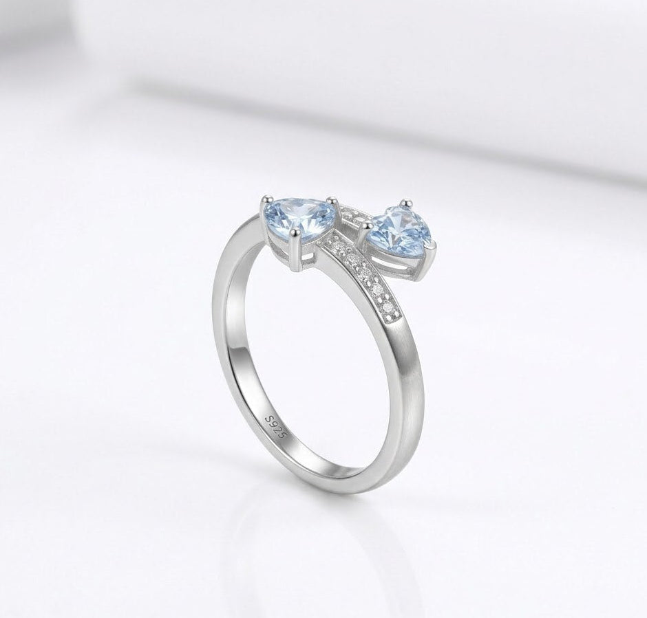 Silver ring with two heart-shaped blue gemstones on a white background