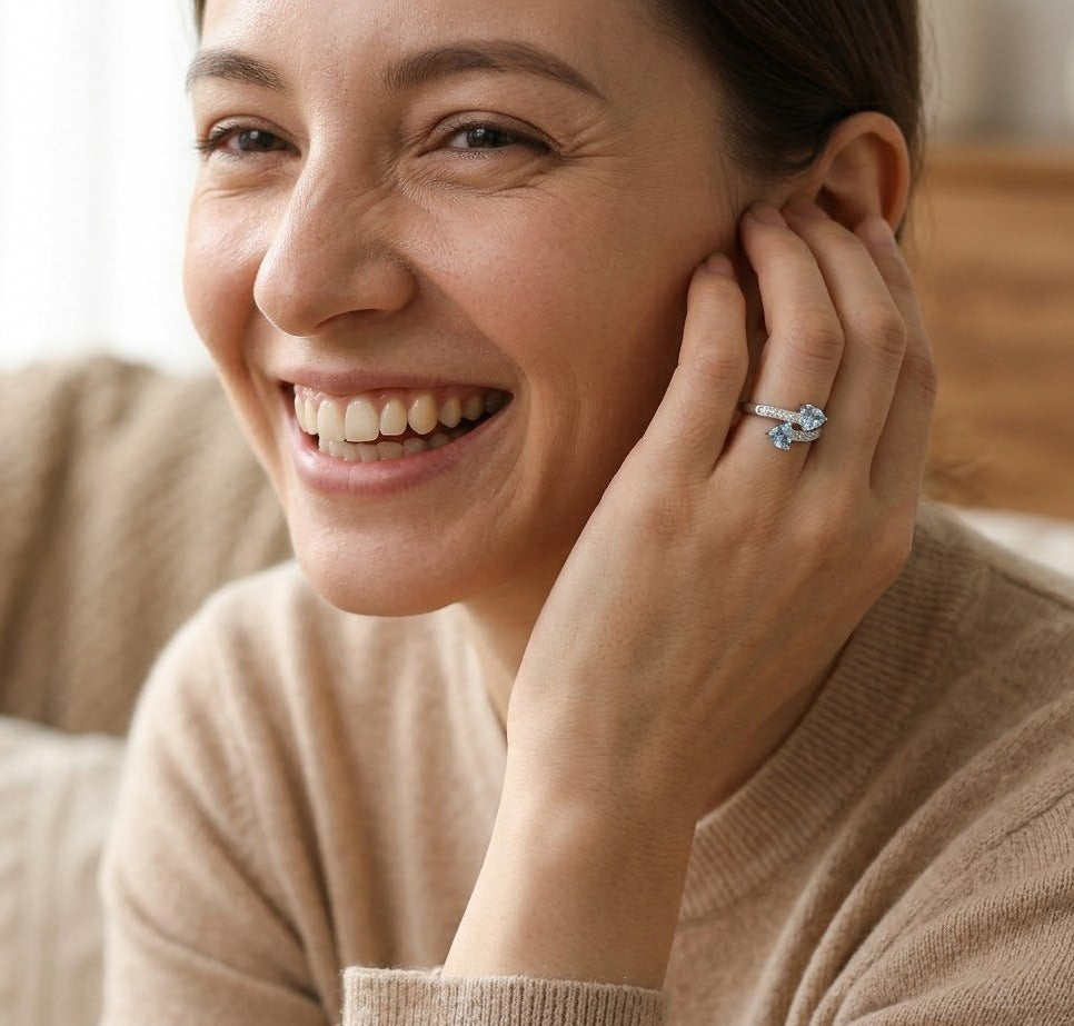 Woman wearing a ring, smiling and touching her ear.