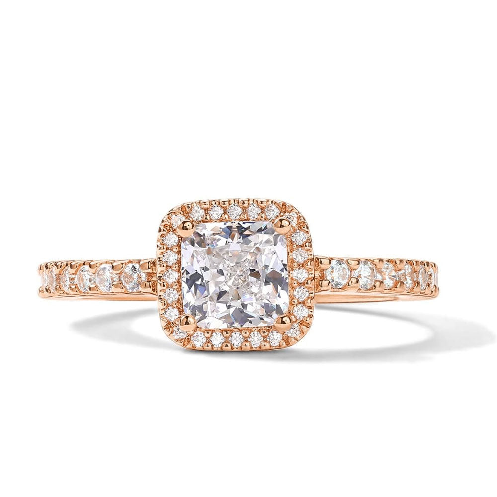 The Cushion Cut Moissanite Ring showcases a cushion-cut center stone with a diamond halo and additional stones along the band, crafted in rose gold—a romantic design inspired by classic promise rings.
