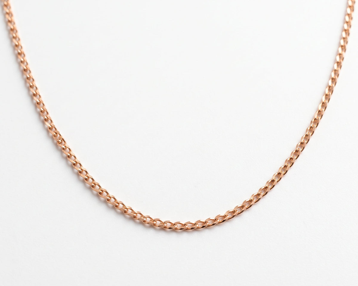 A close-up of a silver gold plated curb chain necklace against a plain white background.