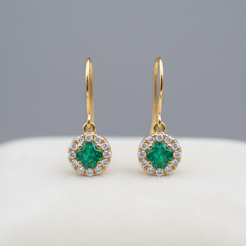 Gold earrings with emerald stones on a light gray background