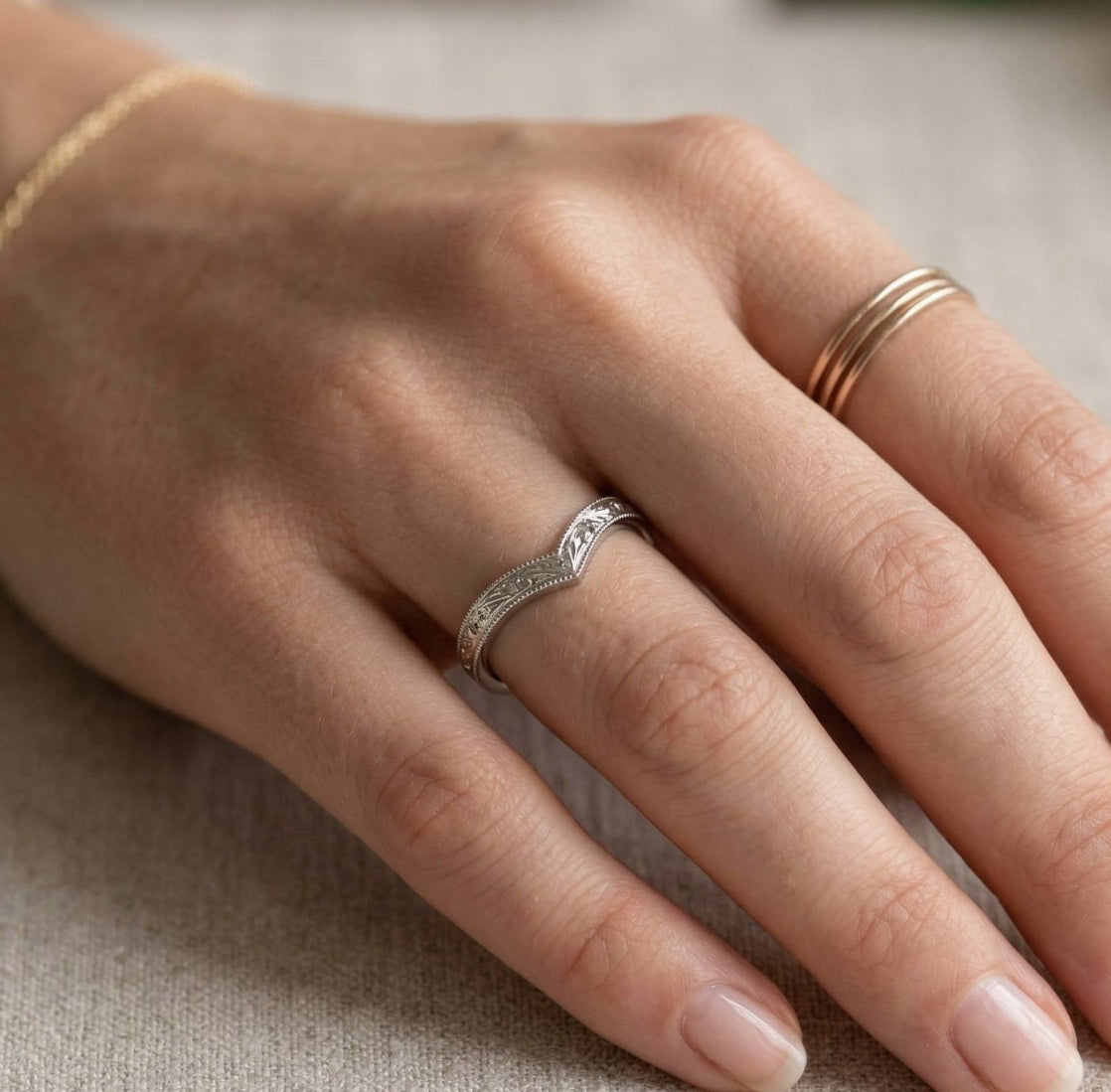 Hand wearing a silver ring with gold bands on a neutral background