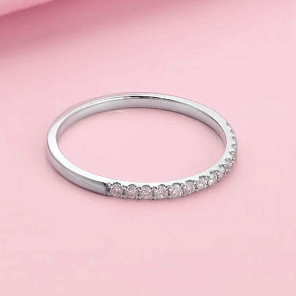 Minimalist silver eternity ring stacked with other bands on rose background