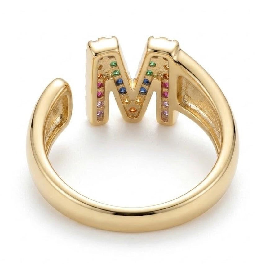A gold-plated open band ring featuring a large letter 'M' adorned with small multicolored gemstones, shown on a clean white background.