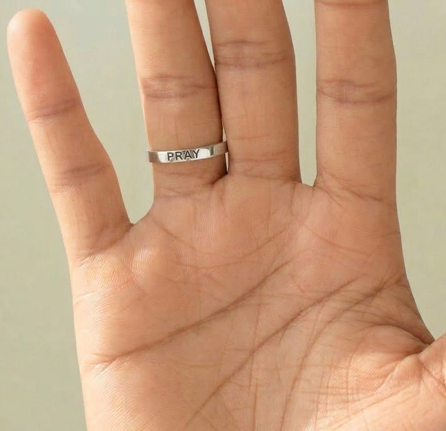 Silver ring with a CZ Pray gravy on a person's finger against a green background
