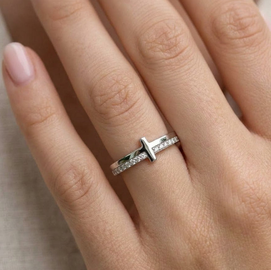 Silver ring with a CZ on a person's finger against a neutral background