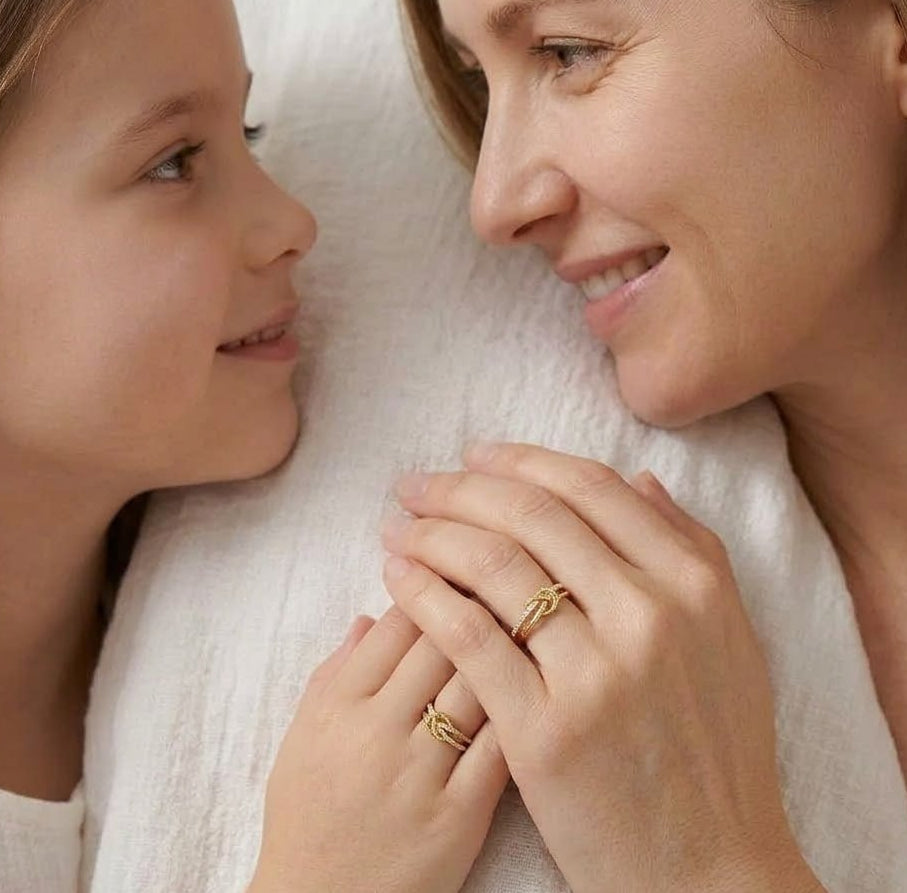 Woman and young girl holding hands with Gold Plated Silver Knot Purity Rings, surrounded by soft white fabric