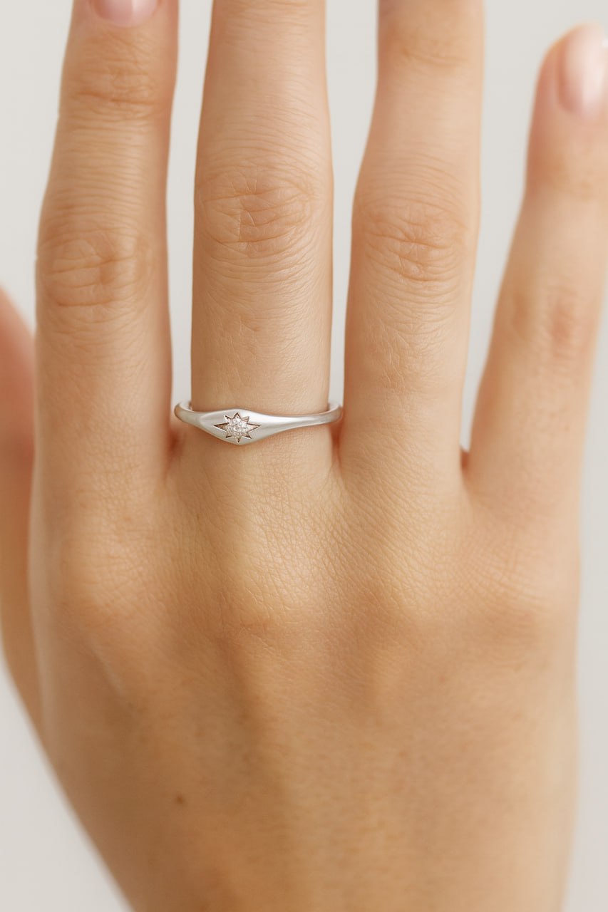 14k white gold  star ring on a person's finger against a neutral background