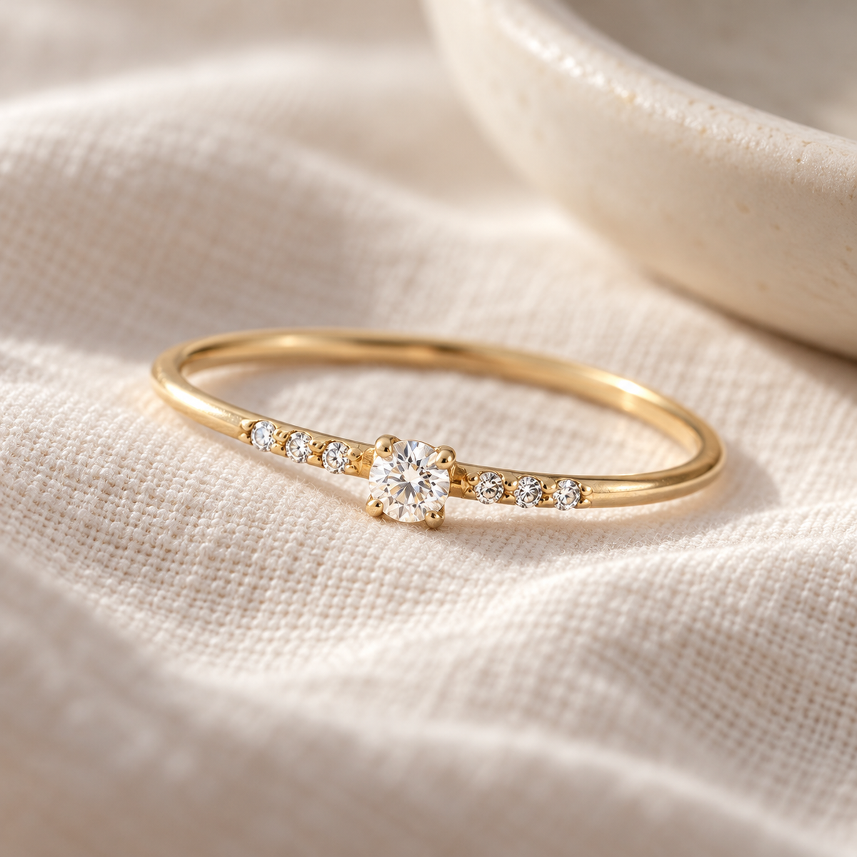 Simple Diamond Ring in yellow gold with a petite center diamond and six side diamonds on ivory linen